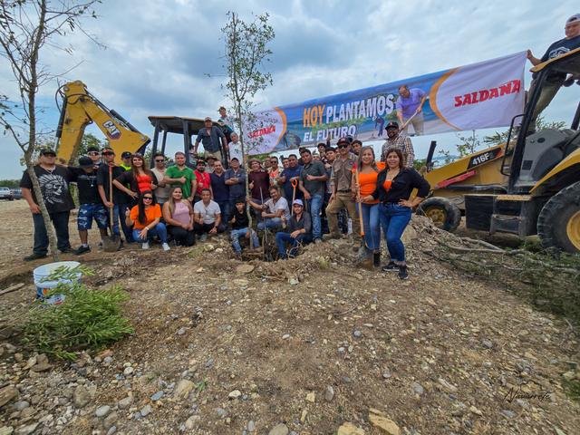 Participantes de la jornada de reforestación en El Coconal junto a árboles, herramientas y maquinaria.