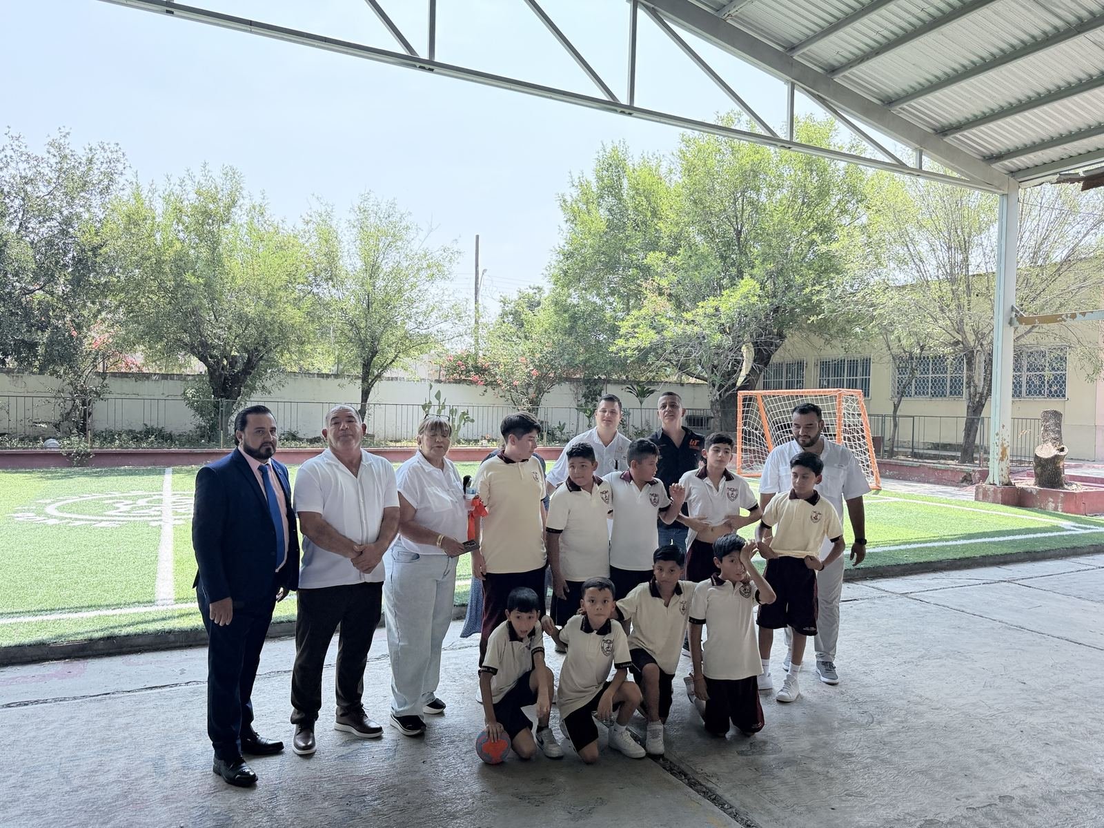 Fotografía grupal de asistentes y alumnos junto a la cancha de fútbol de la primaria.